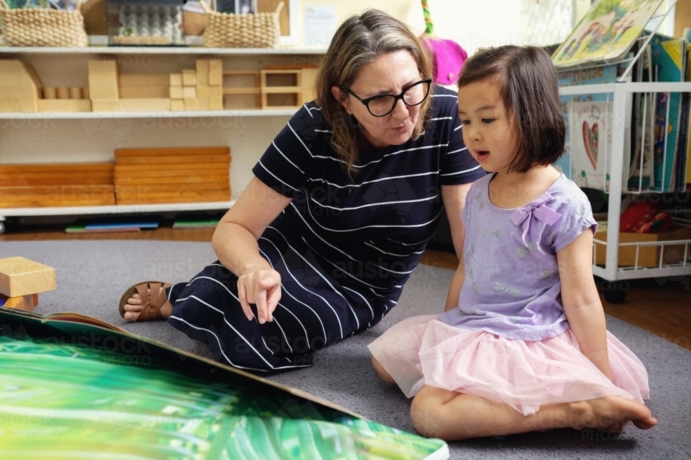 Happy multicultural teacher and child reading a book in kindergarten - Australian Stock Image