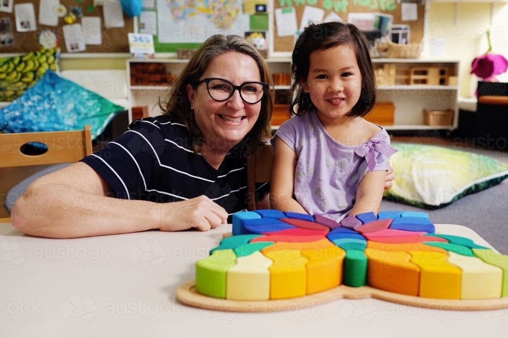 Happy multicultural teacher and child with wooden blocks puzzles in kindergarten - Australian Stock Image