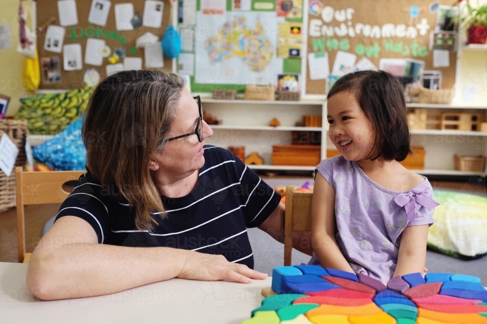 Happy multicultural teacher and child with wooden blocks puzzles in kindergarten - Australian Stock Image