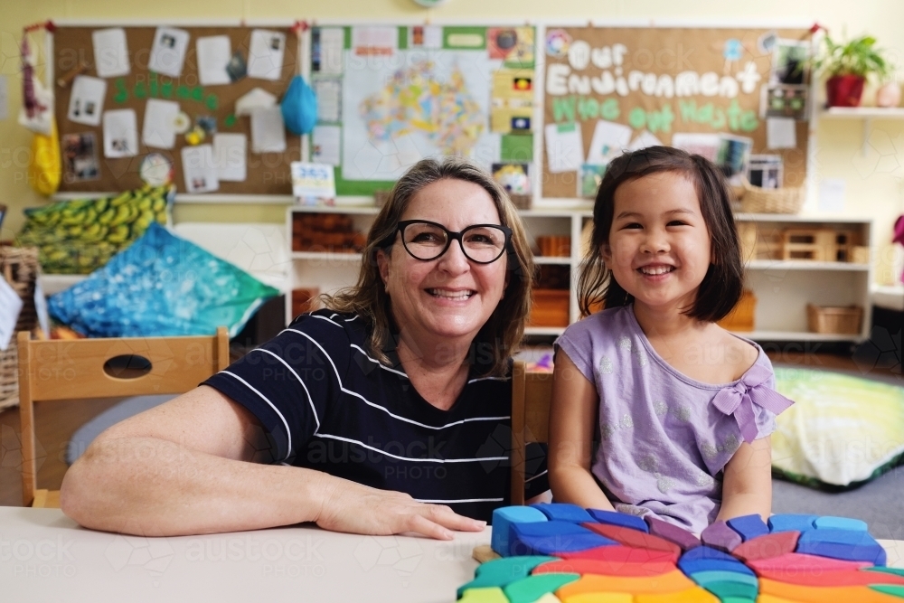Happy multicultural teacher and child with wooden blocks puzzles in kindergarten - Australian Stock Image