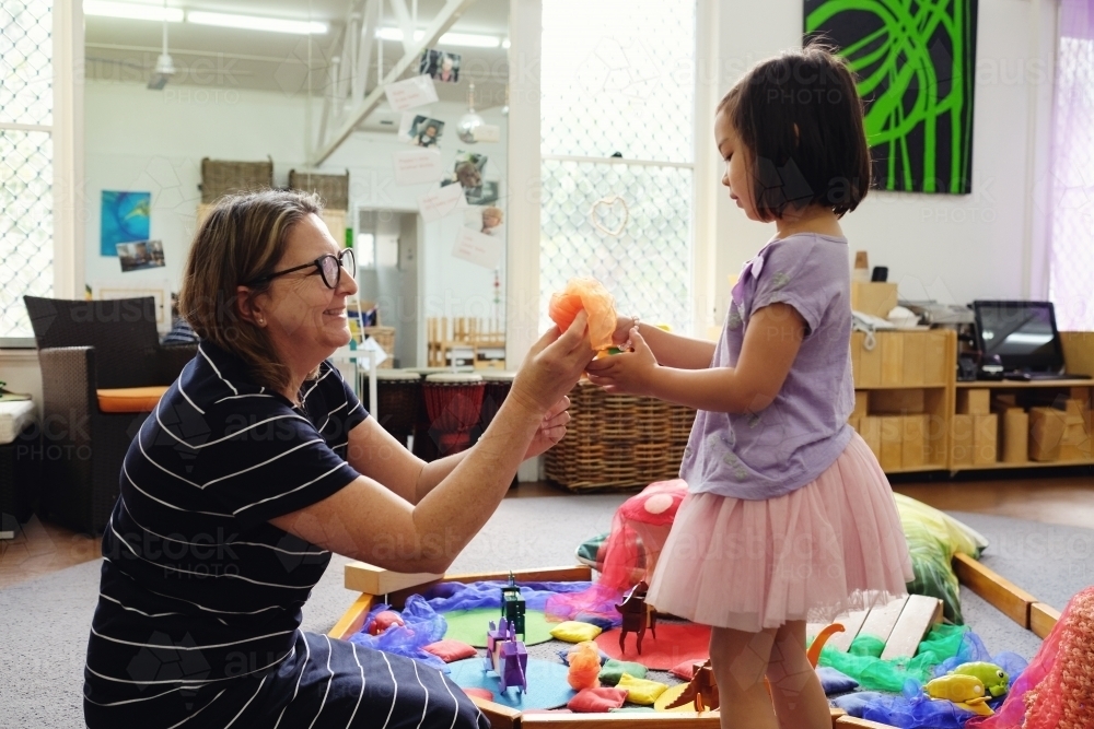 Happy multicultural teacher and child with wooden blocks puzzles in kindergarten - Australian Stock Image