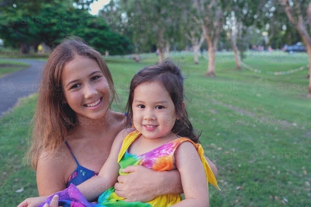 Happy multiethnic teenage girl holding little girl in the park - Australian Stock Image