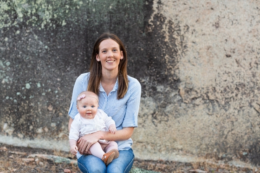 Happy mum and baby sitting outdoors on a rock - Australian Stock Image