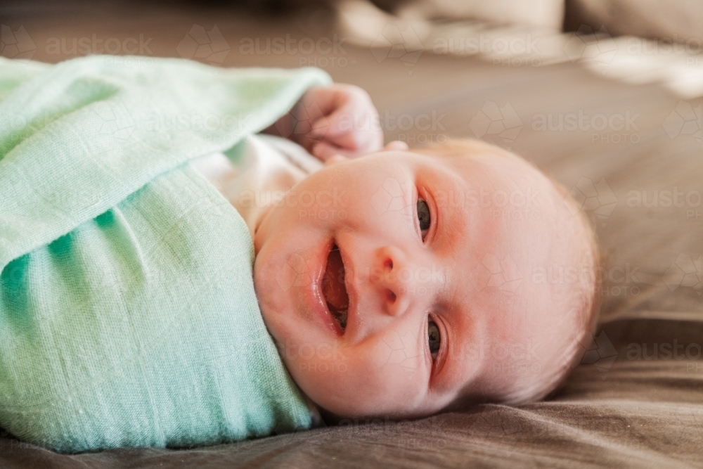 Happy newborn baby in blanket on bed - Australian Stock Image