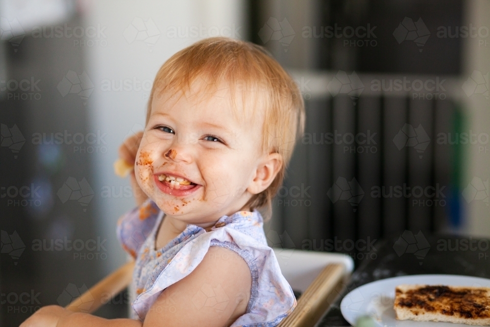 Image of Happy one year old eating toast food with messy face