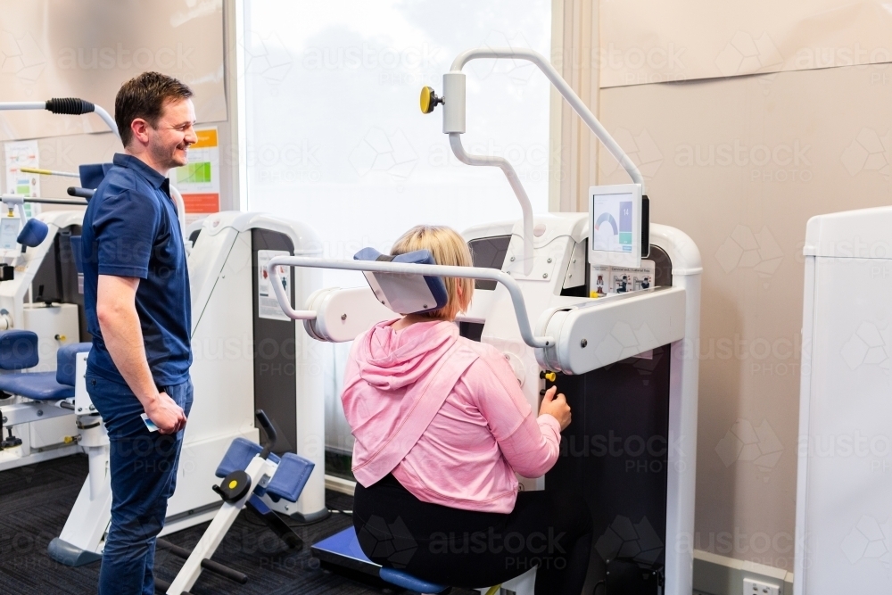 Happy physio standing beside woman using physical therapy equipment - Australian Stock Image
