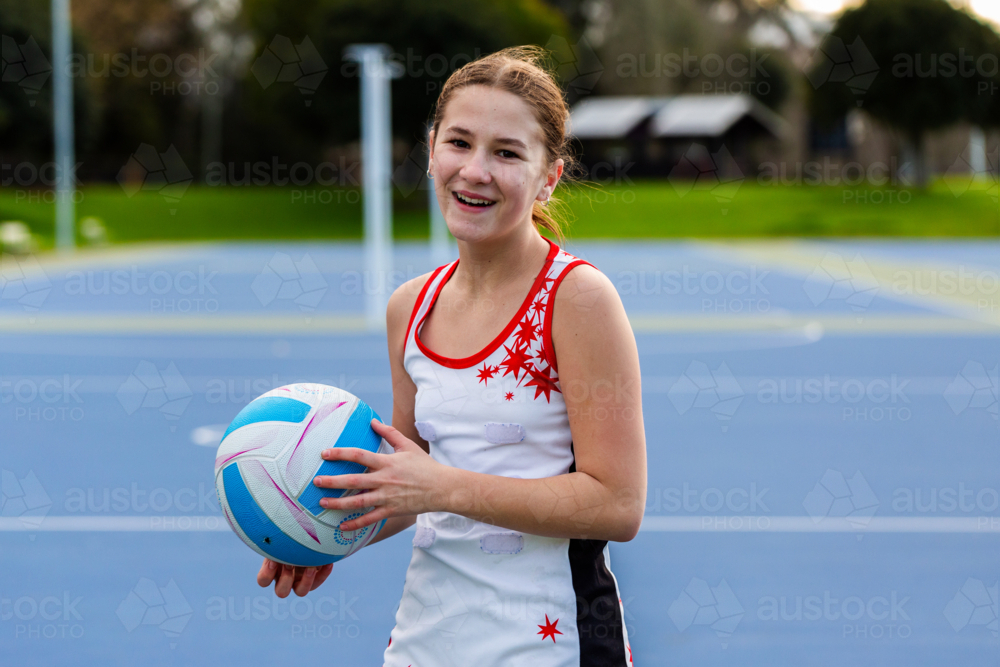 happy pre-teen netball player with ball on court training for sports game - Australian Stock Image