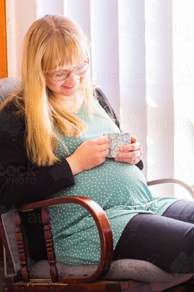 Image of Happy pregnant woman sitting in rocking chair with mug of ...