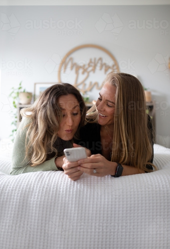 Happy same sex couple lying on a bed looking at a smart phone - Australian Stock Image