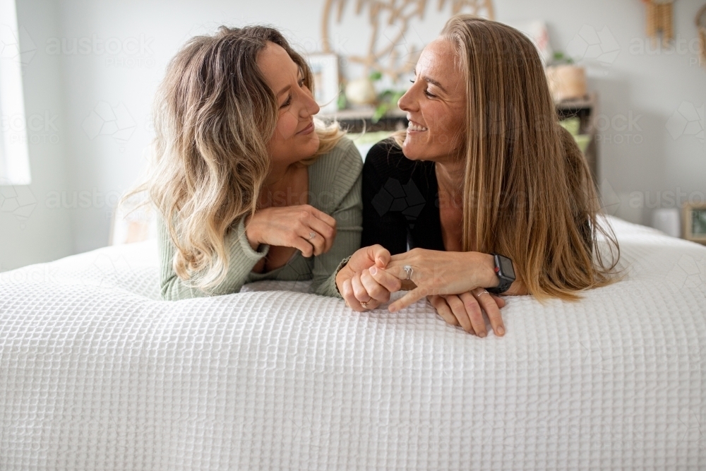 Happy same sex couple lying on a bed looking at one another - Australian Stock Image