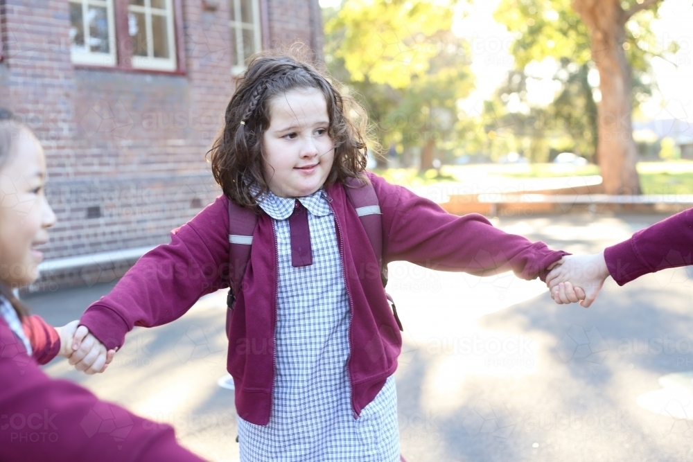 Happy school children holding hands and playing in the school yard - Australian Stock Image