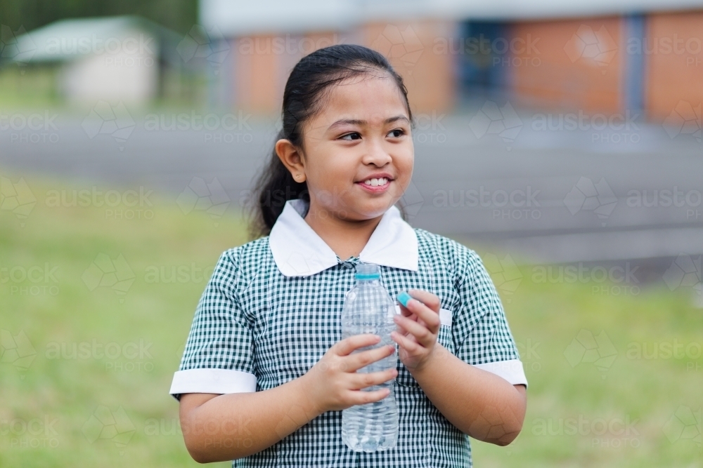 Happy school girl holding plastic water bottle - Australian Stock Image
