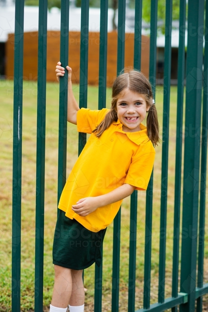 Happy school girl swinging off the school fence - Australian Stock Image