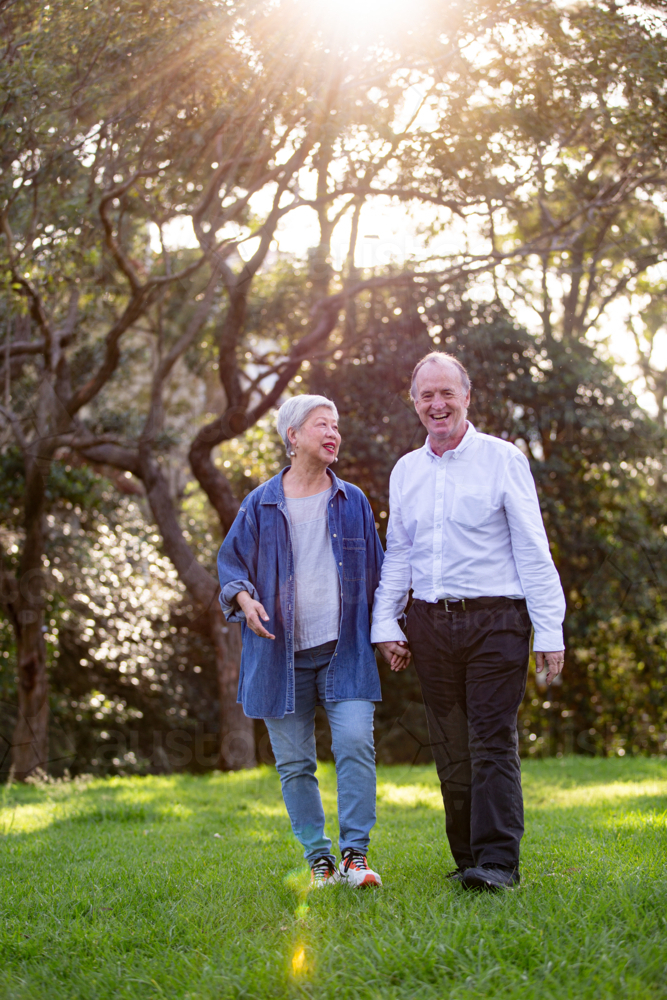 Happy senior couple walking at the grass field in public park - Australian Stock Image