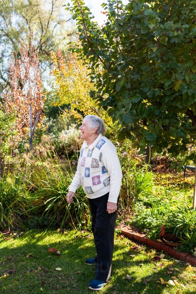 Happy senior woman standing in garden outside on winter morning laughing - Australian Stock Image
