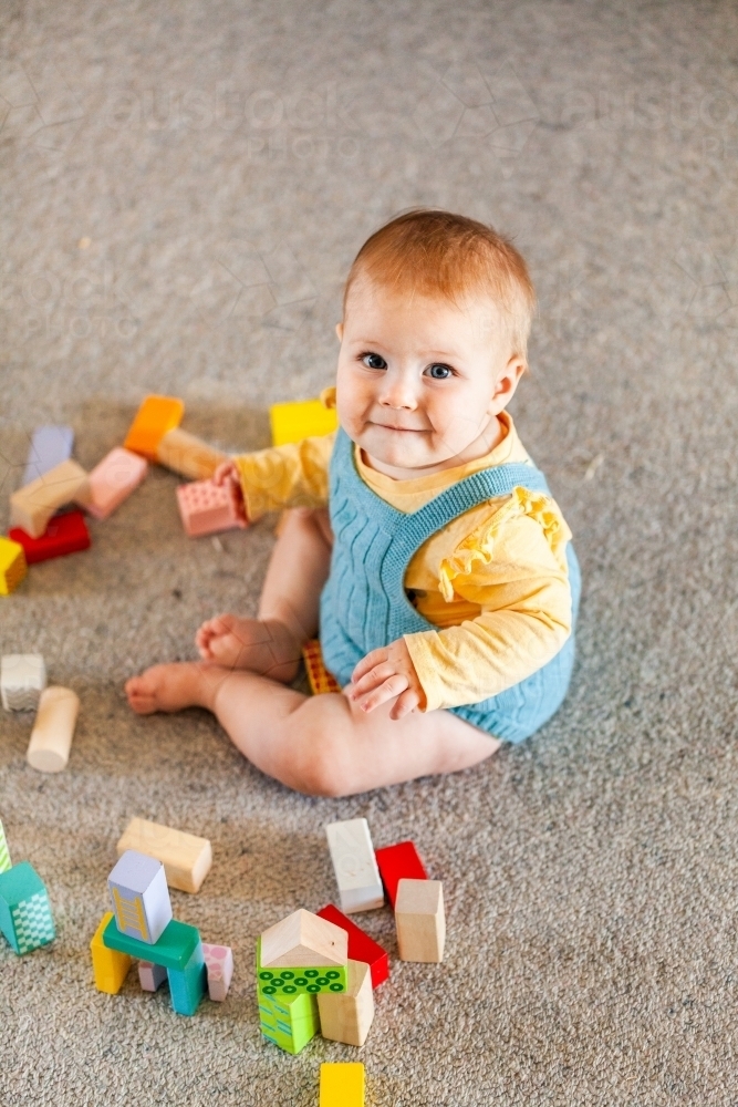 Happy seven month old baby playing with coloured blocks on carpet floor - Australian Stock Image