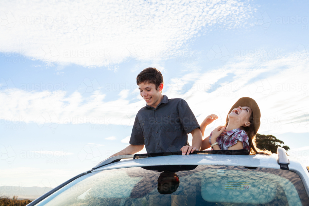 Happy siblings looking out car sunroof with bright sky on road trip adventure at lookout - Australian Stock Image