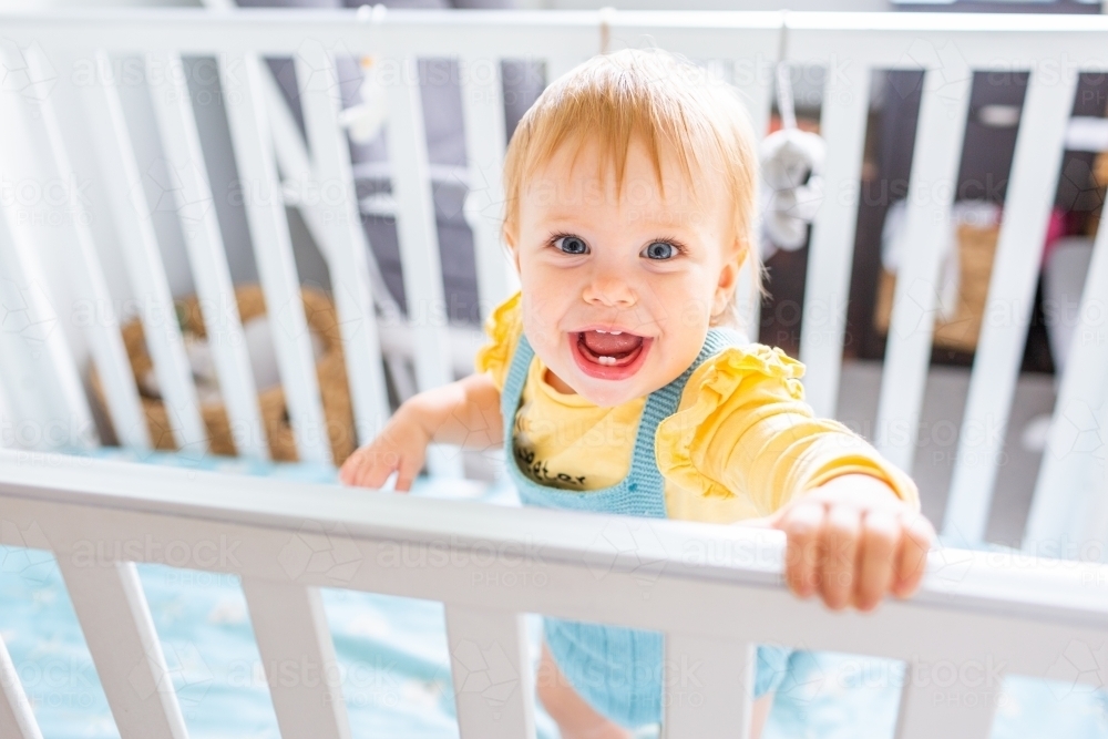 Happy smiling baby standing up in cot - Australian Stock Image