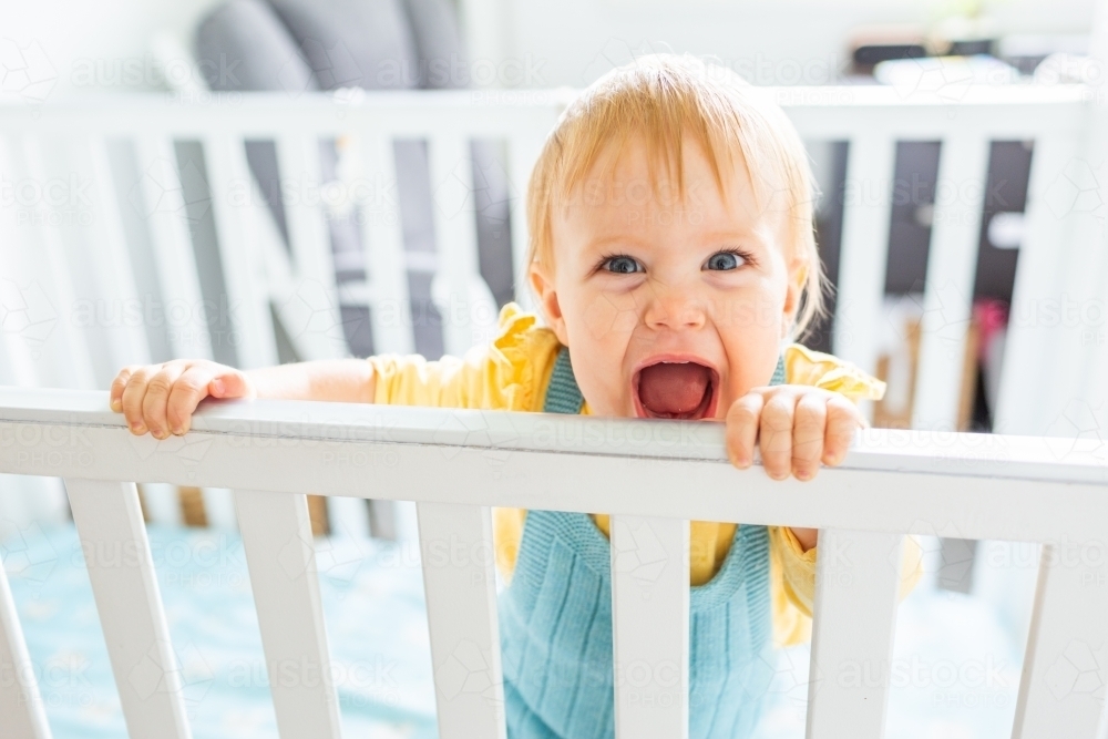 Happy smiling baby standing up in cot - Australian Stock Image
