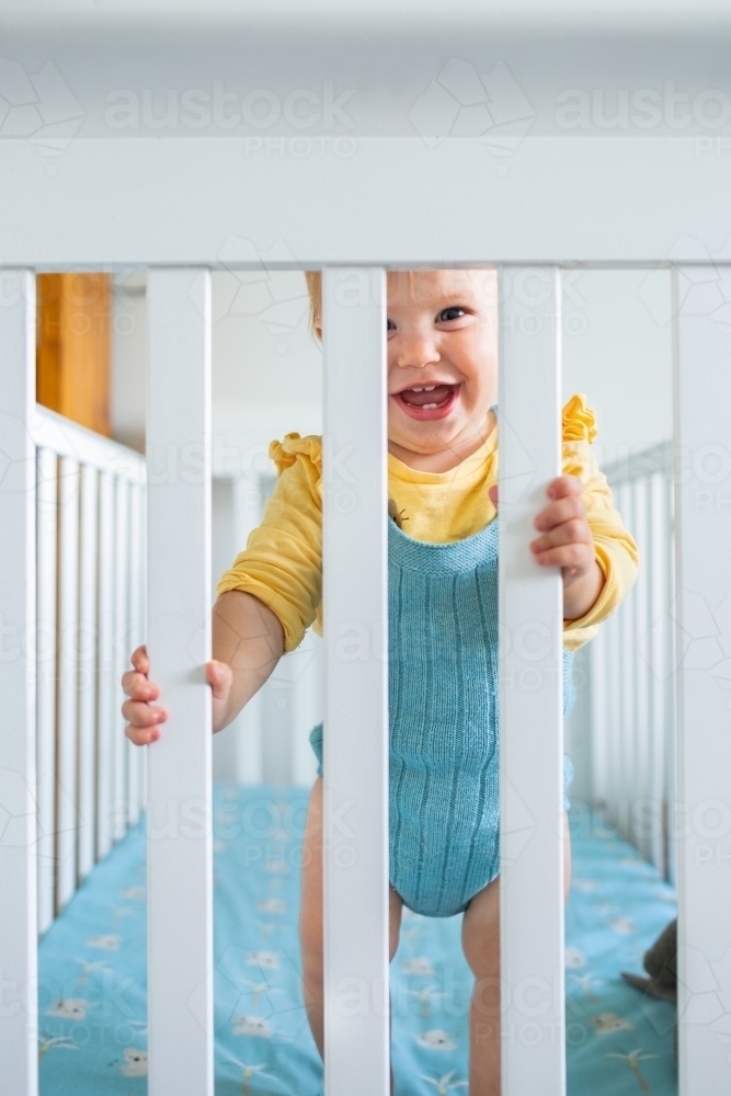 Happy smiling baby standing up in cot - Australian Stock Image