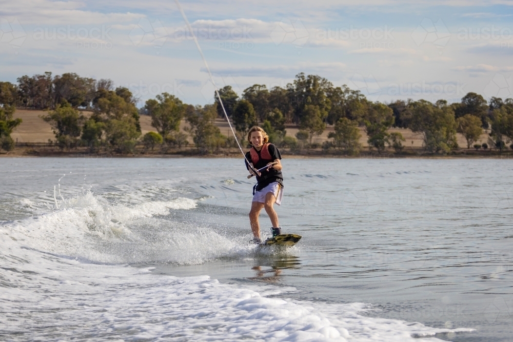 happy smiling boy on wake board on lake - Australian Stock Image