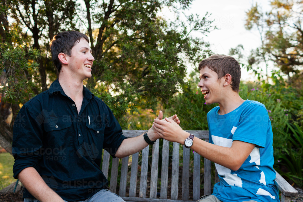 Happy smiling brothers playing hand slapping game outside in backyard - Australian Stock Image