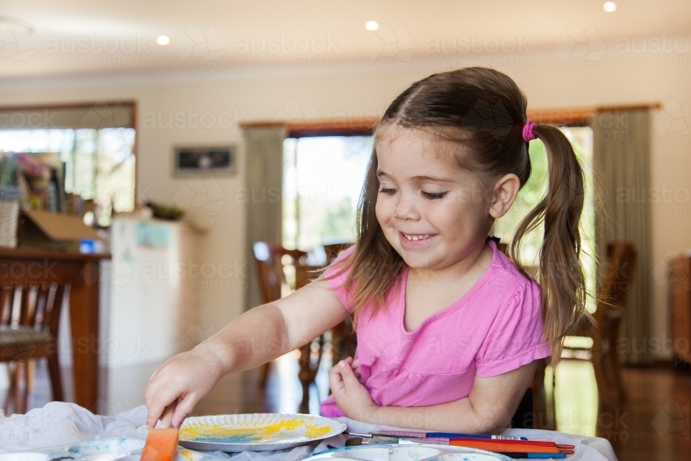 Happy smiling girl painting a picture in pre-school - Australian Stock Image