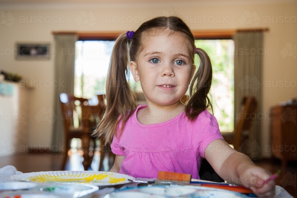 Happy smiling girl painting a picture in pre-school - Australian Stock Image