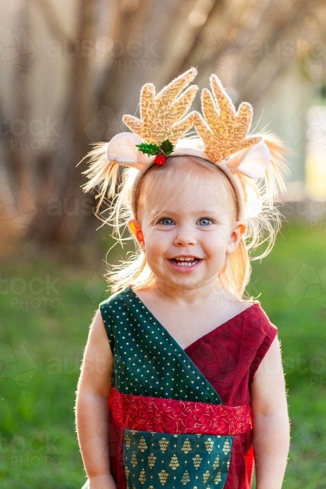 Happy smiling little girl in Christmas colours and wearing deer antler headband - Australian Stock Image
