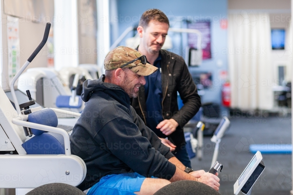 happy smiling male physio client with physiotherapist using exercise therapy equipment - Australian Stock Image