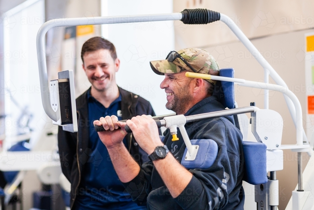 happy smiling male physio client with physiotherapist using exercise therapy equipment - Australian Stock Image