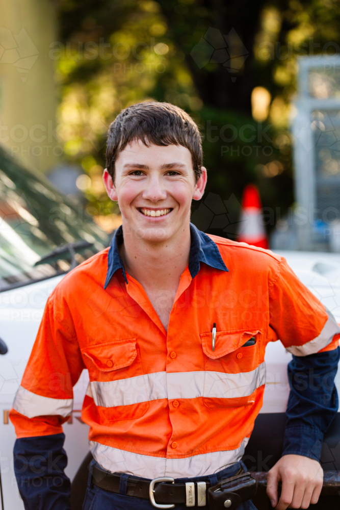 happy smiling portrait of young male trade apprentice person in high-vis workwear beside vehicle - Australian Stock Image