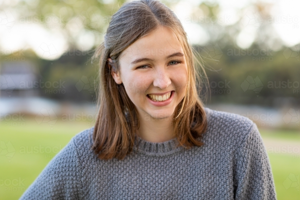 happy smiling teenager wearing grey sweater outdoors - Australian Stock Image