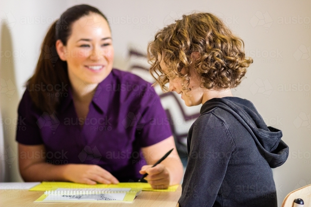 Happy speech therapist reading with child in clinic - Australian Stock Image