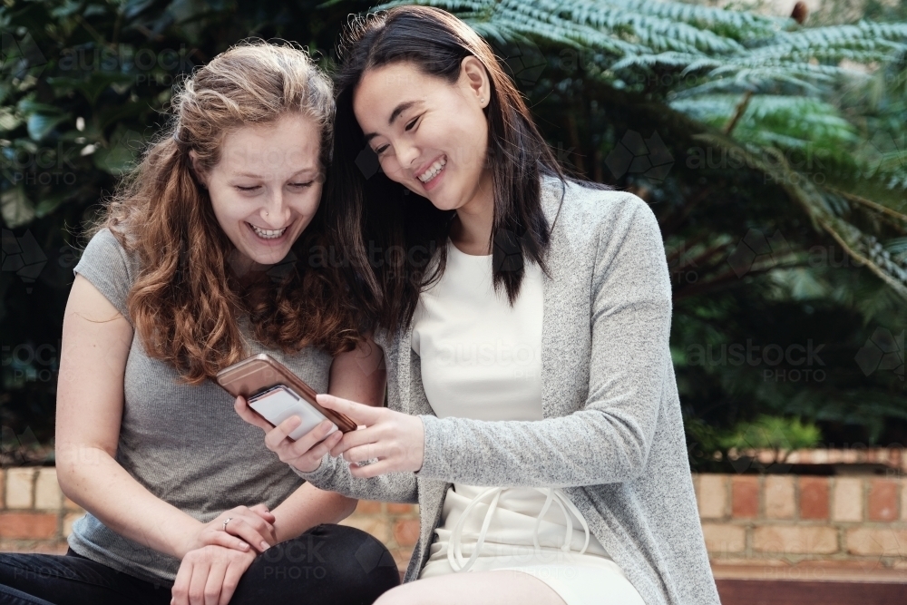 Happy students girl friends using mobile - Australian Stock Image