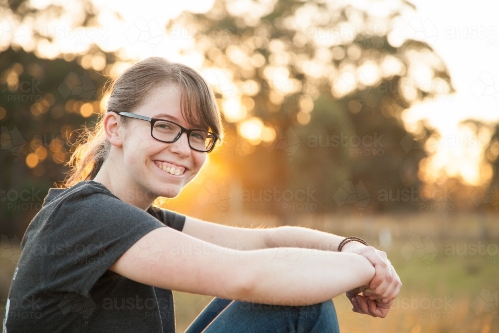 Happy teen girl sitting outside in the paddock - Australian Stock Image