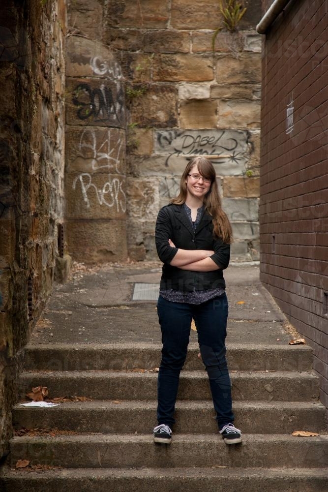 Happy teen girl standing confidently on steps in an alleyway - Australian Stock Image