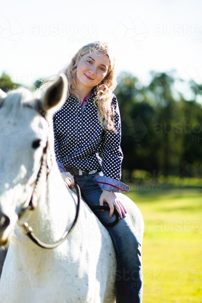Happy teen person riding her horse in sunlit paddock - Australian Stock Image