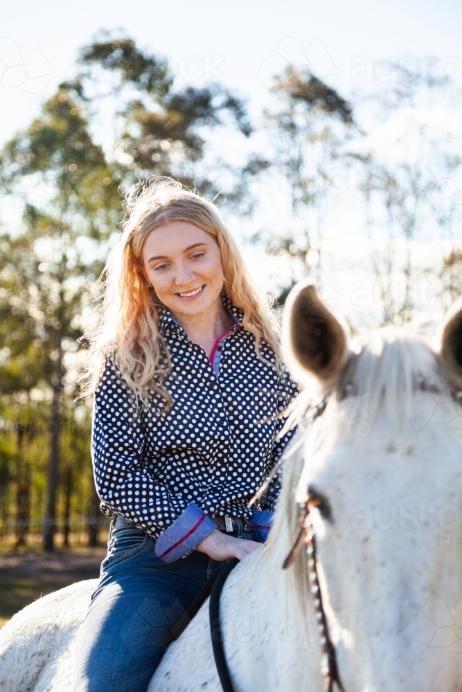 Happy teen person riding her horse in sunlit paddock - Australian Stock Image
