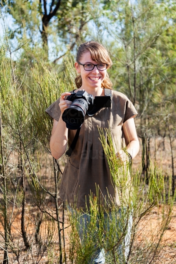 Happy teen photographer standing among trees - Australian Stock Image
