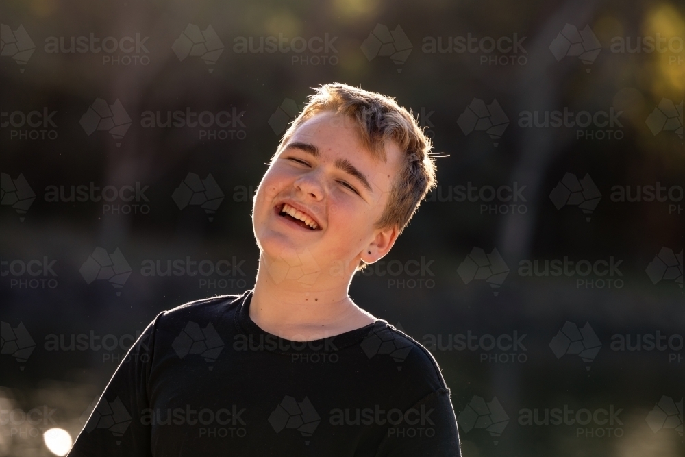 Happy teenage boy by the water in golden afternoon sunshine - Australian Stock Image