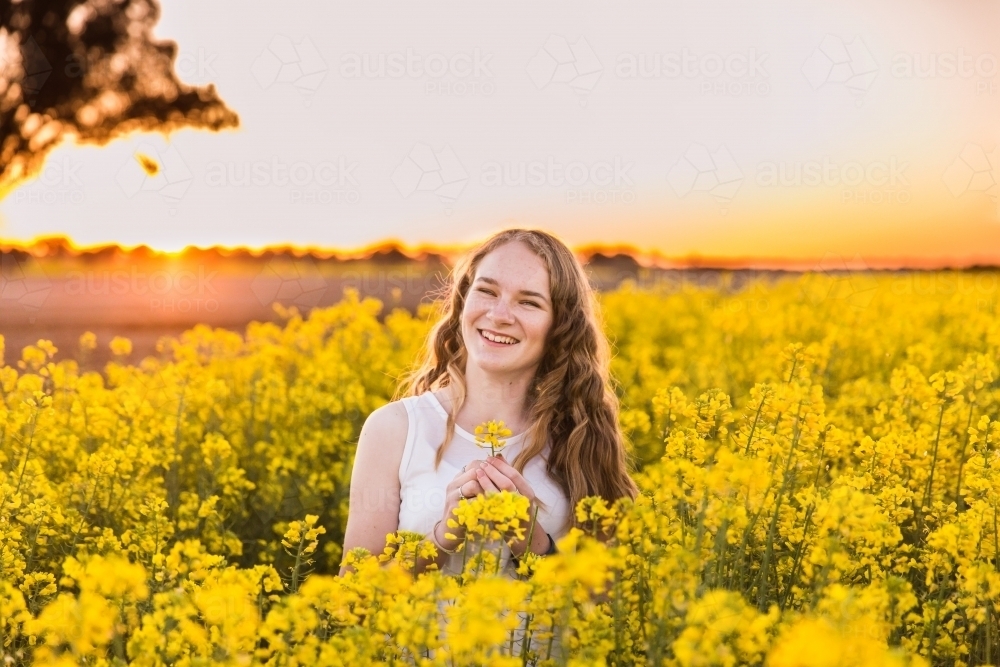 Happy teenage girl on farm in canola field at sunset - Australian Stock Image