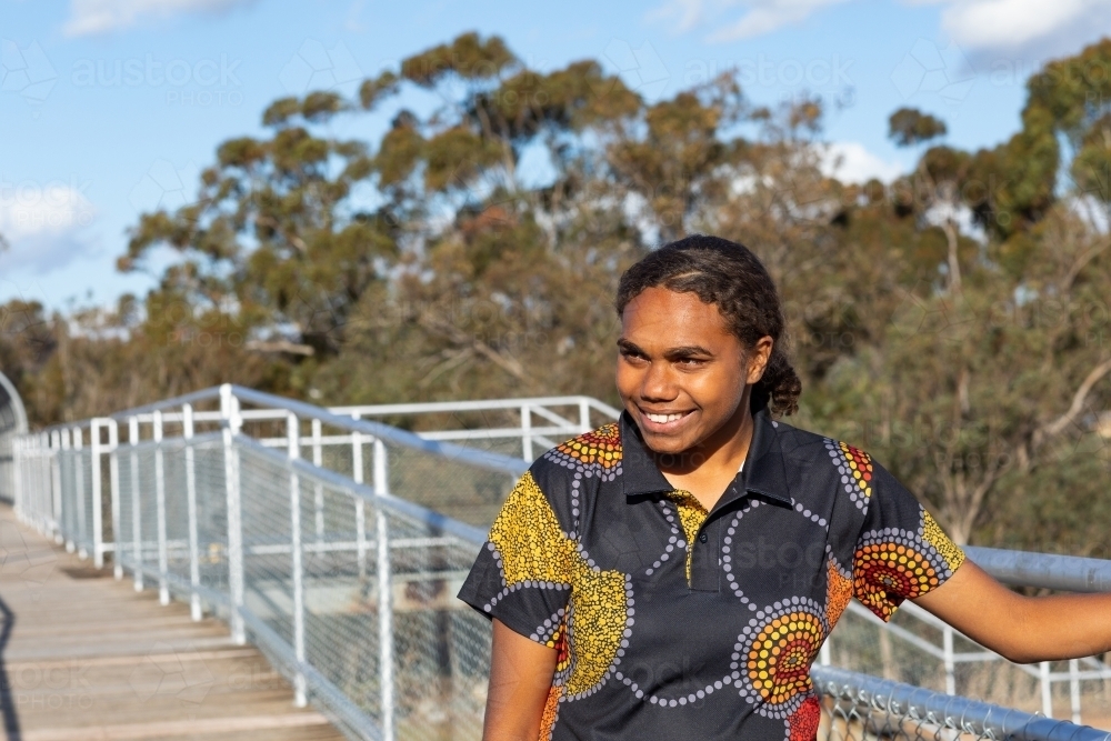 happy teenage girl on footbridge with trees in background - Australian Stock Image