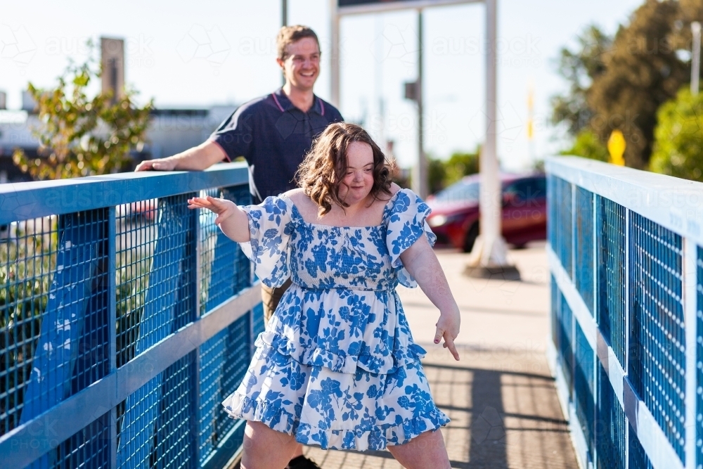 Happy teenage girl with down syndrome dancing on blue footbridge - Australian Stock Image