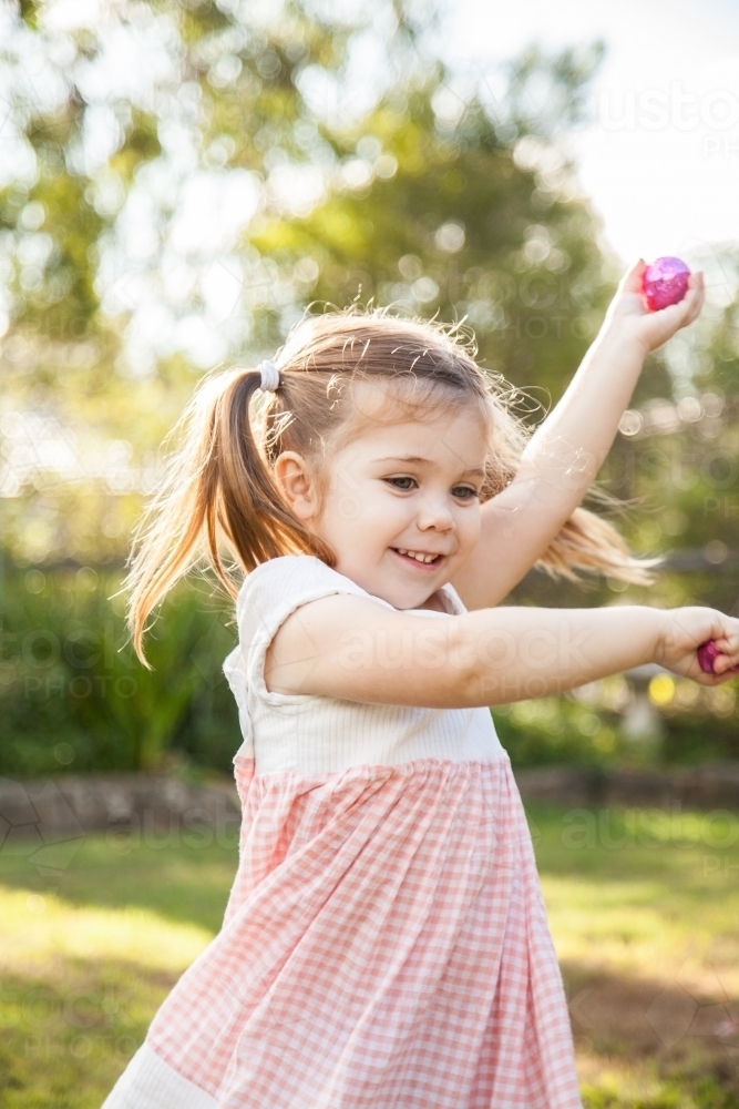 Happy three year old child spinning with Easter eggs she found - Australian Stock Image