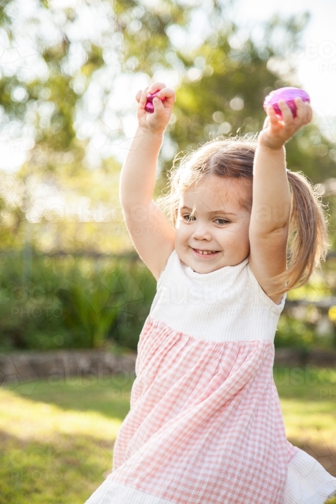 Happy three year old child spinning with Easter eggs she found - Australian Stock Image