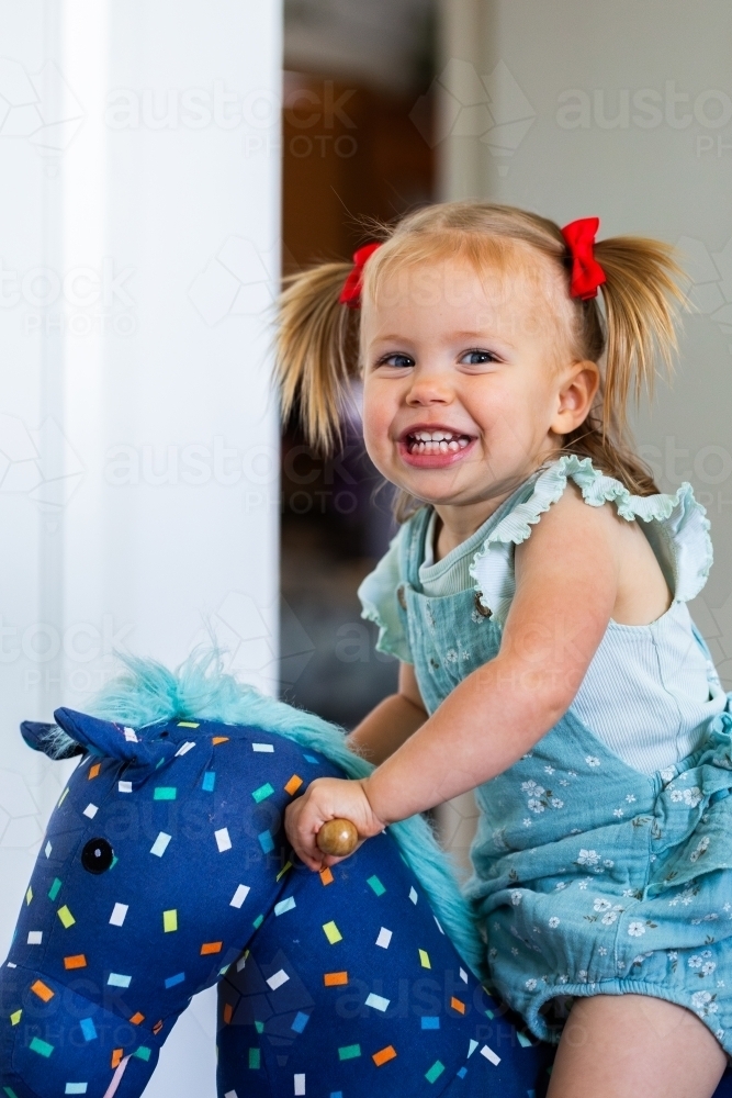 Happy toddler girl riding on rocking horse toy - Australian Stock Image