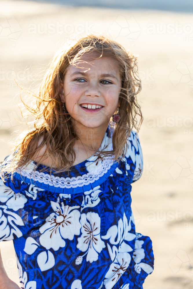 Happy Torres Strait Islander girl at beach on windy day wearing traditional floral dress - Australian Stock Image