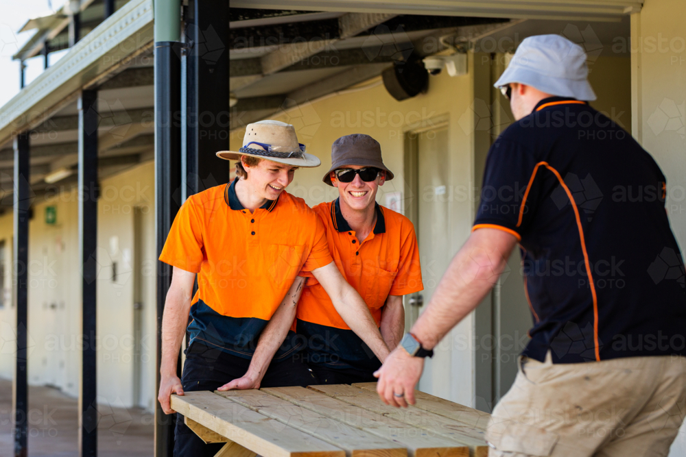 Image of Happy trade apprentices moving table they built during hands ...