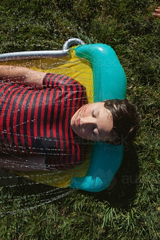 Happy tween boy lying in a sprinkler on a hot summer's day - Australian Stock Image